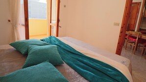 Une chambre à coucher avec un lit, des oreillers, une fenêtre et une porte donnant sur un balcon.
