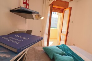 Une pièce avec un lit, un livre intitulé « Il Grande Salento per immaginati – Otranto », une étagère avec une lampe et une porte donnant sur l’extérieur.