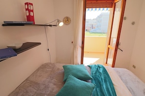 Un dormitorio con cama, almohadas, una estantería con libros, un reloj de pared y vistas al exterior.