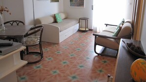 Un espace de vie compact comprenant un canapé, un fauteuil, une petite table et une lampe.