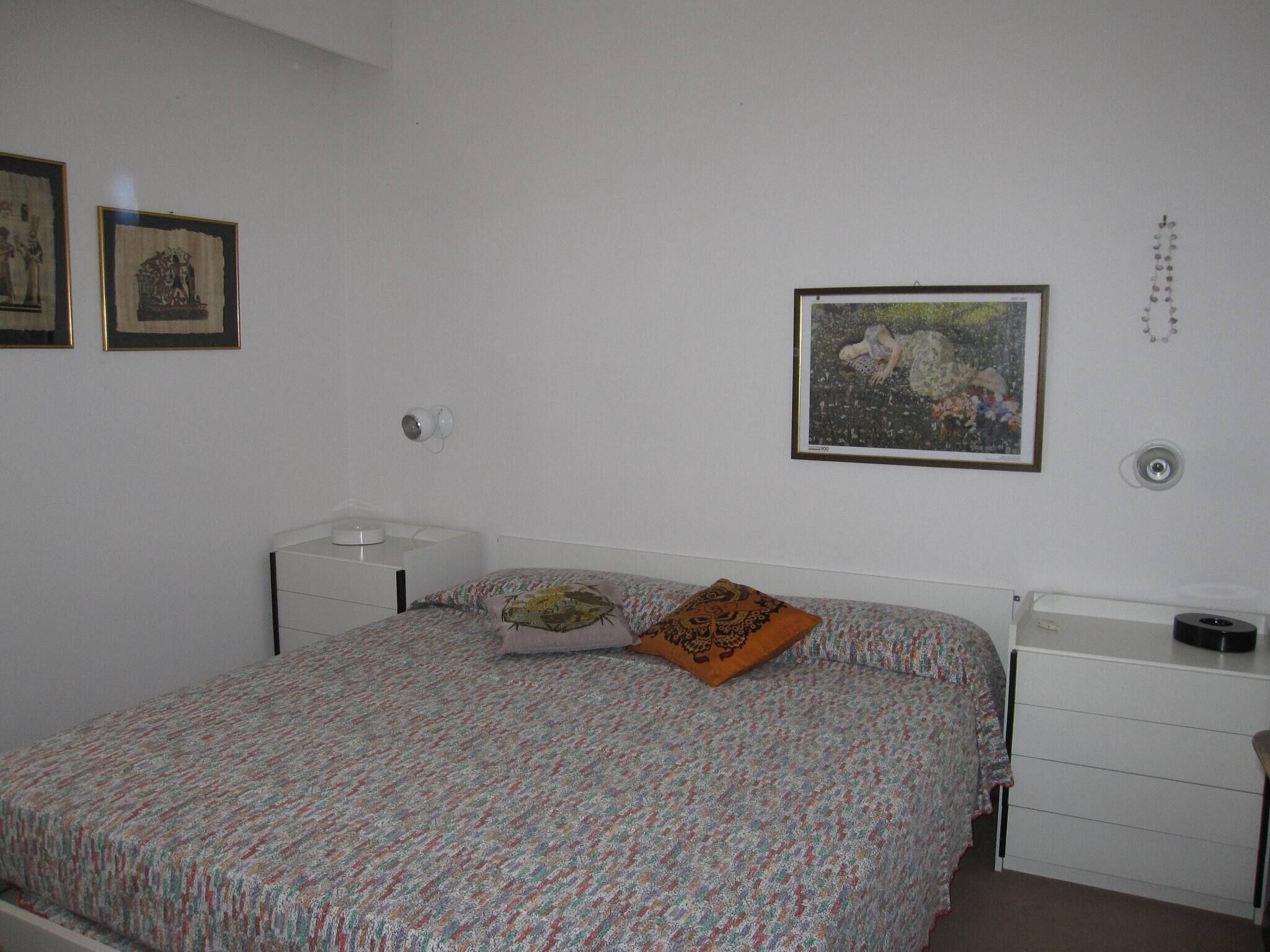 A bedroom with a bed, a bedside table, a nightstand, and a wall-mounted lamp.