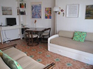A living room with a sofa, a dining table with chairs, a TV, and artwork on the walls. - Wonderful Seaview Flat With Terrace (Grado)