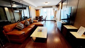 A modern living room with a leather sofa, a coffee table, and a TV. - 6C - 2 Bedroom Downtown Apartment With Shared Pool (Bangkok)