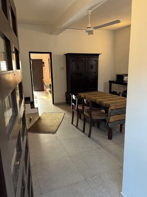 Une pièce comprenant une table à manger, des chaises, un buffet en bois foncé, un ventilateur de plafond et une porte donnant sur une autre pièce.