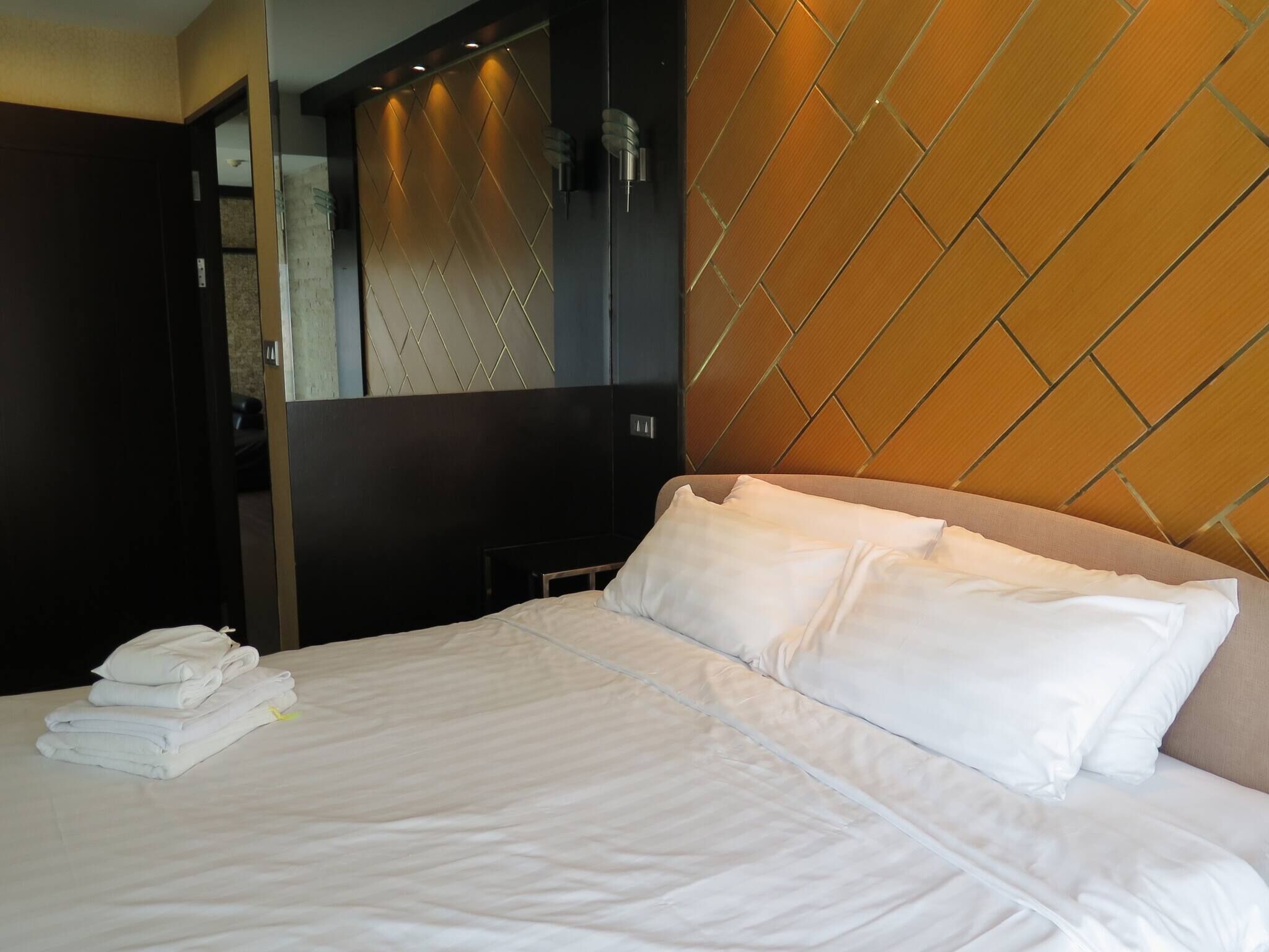 A hotel room with a bed, a mirror, and a wall with a geometric pattern.
