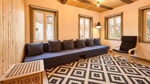 A room with a wooden ceiling, a sofa with cushions, a chair, and patterned carpet.