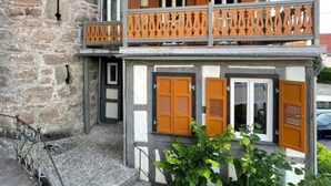 A two-story building with a stone facade, wooden shutters, and a balcony with a metal railing.