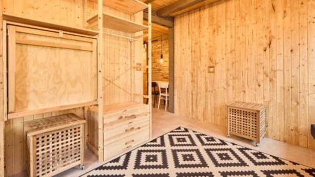 A wooden interior with a built-in bench, a patterned rug, and a small wooden cabinet.