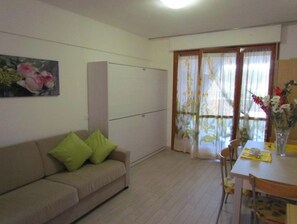 Une pièce comprenant un canapé, une table à manger avec des chaises, un meuble et une fenêtre avec des rideaux.