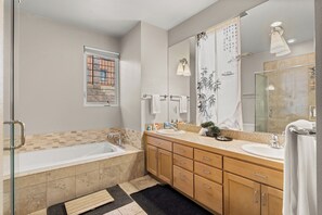 Enjoy a spacious bathroom with a large bathtub, separate sink area, glass-enclosed shower, and large mirror.