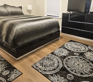 A bedroom with a bed, a dresser, a television, and patterned rugs.