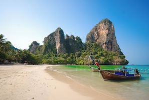 A beach with boats, clear water, and a large rock formation. - B201 - 1 Bedroom Condo With Sea View, Ao Nang Beach (Krabi)