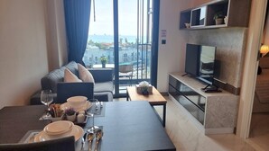 A modern hotel room with a dining area, a sofa, a TV, and a balcony with a city view. - B201 - 1 Bedroom Condo With Sea View, Ao Nang Beach (Krabi)