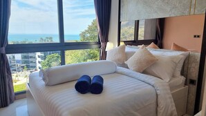 A bedroom with a large window, a bed with white linens, and a view of the sea and buildings. - B201 - 1 Bedroom Condo With Sea View, Ao Nang Beach (Krabi)