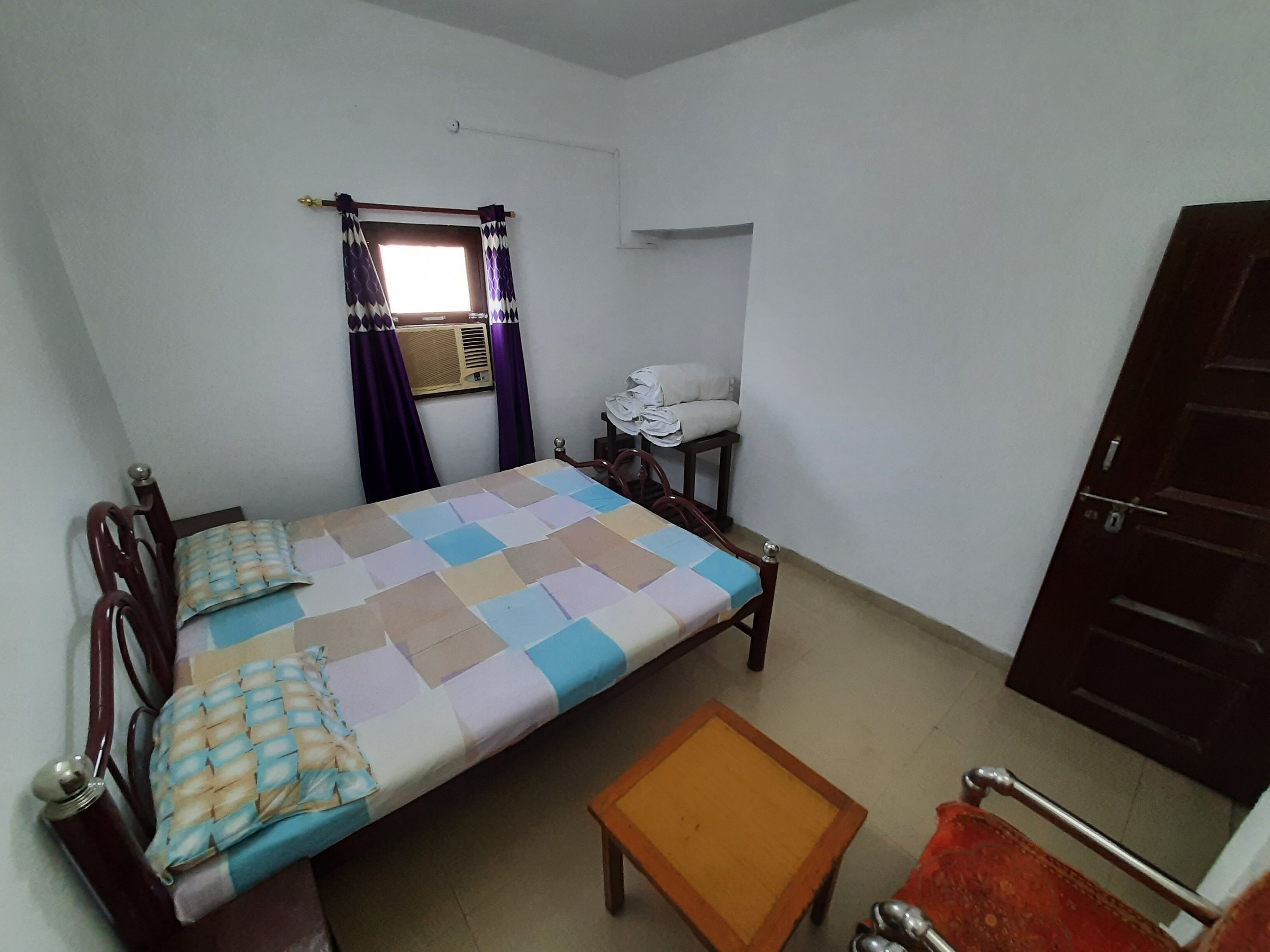 A small, simple room with a bed, a small table, a chair, and a wardrobe.