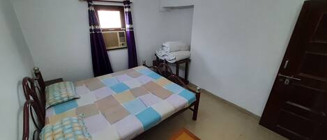 A small, simple room with a bed, a small table, a chair, and a wardrobe.
