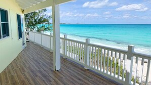 A covered porch with a wooden floor and white railings overlooking a turquoise ocean. - Private Beachfront Home (Great Harbour Cay)