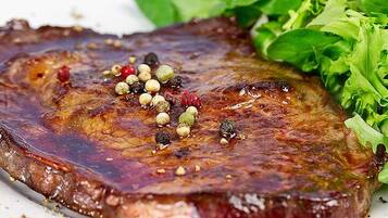 A steak with a glossy, caramelized crust, garnished with peppercorns and herbs, served with a side of green salad.