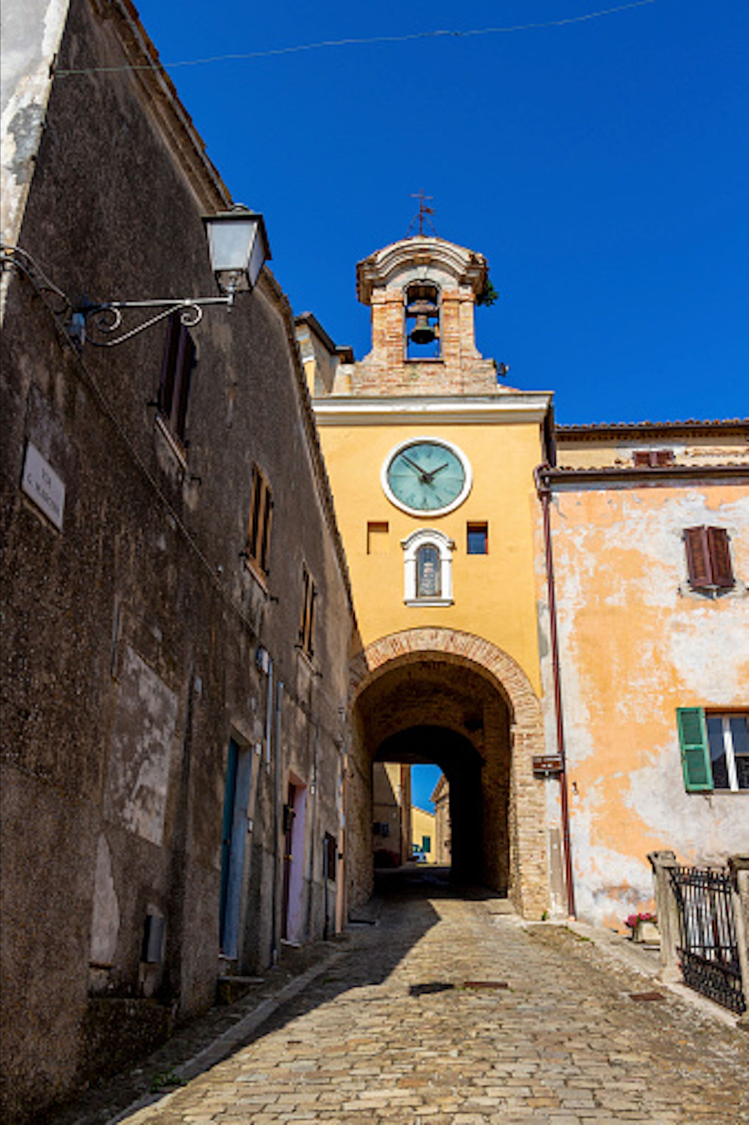 Una estrecha calle adoquinada con edificios históricos, una torre del reloj y un pasaje en arco.