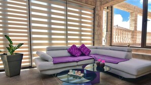 A modern living room with a sectional sofa, a glass coffee table, and a potted plant. - Elegant Huge Villa Large Pool, Ideal For Weddings (Kathikas)