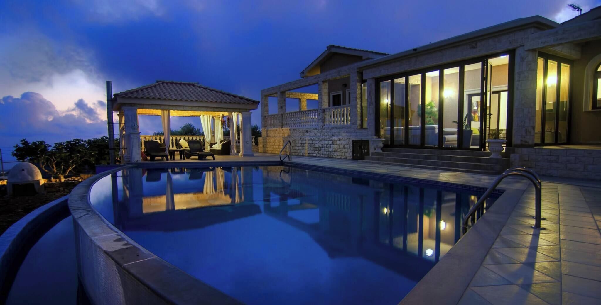 A swimming pool with a gazebo, a covered patio, and a house with large windows.
