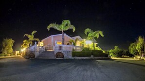 A well-lit, two-story house with a gated entrance, palm trees, and a stone pathway leading to the driveway. - Elegant Huge Villa Large Pool, Ideal For Weddings (Kathikas)
