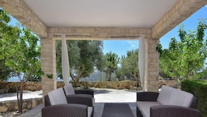A covered outdoor seating area with wicker furniture and a stone wall backdrop. - Elegant Huge Villa Large Pool, Ideal For Weddings (Kathikas)