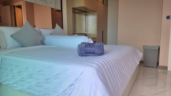 A neatly made bed with a striped bedspread and pillows, a folded towel, and a trash bin to the side. - Bo401 - 2 Bdr Condo With Sea View, Ao Nang Beach (Krabi)