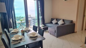 A dining area with a table set for four, a grey sofa, and a view of the ocean through large windows. - Bo401 - 2 Bdr Condo With Sea View, Ao Nang Beach (Krabi)