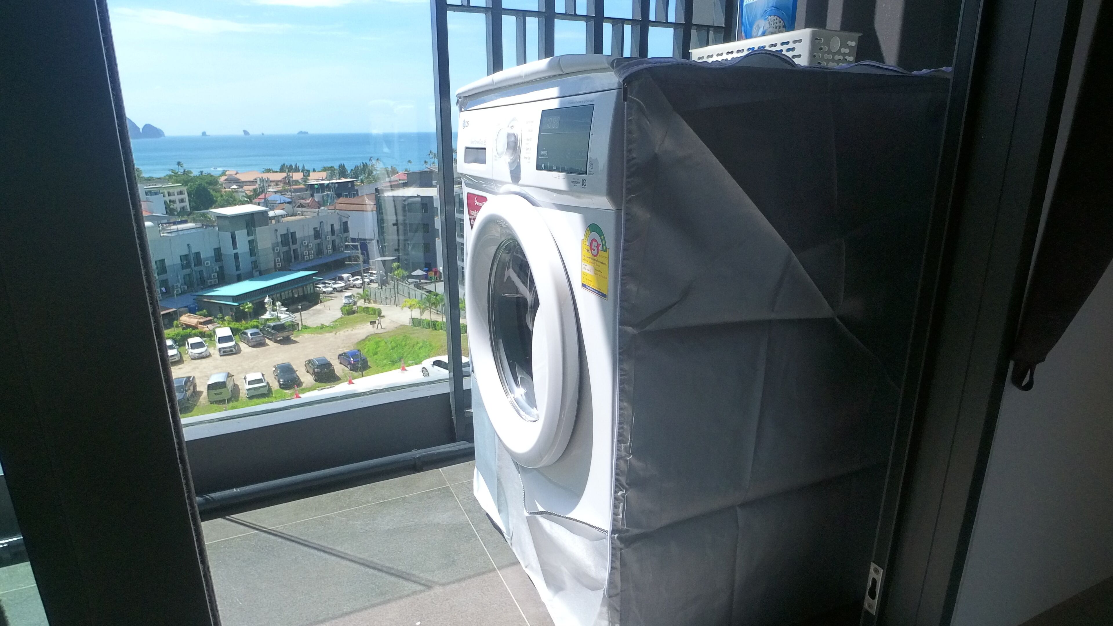Une machine à laver dans une pièce donnant sur un parking et des immeubles.