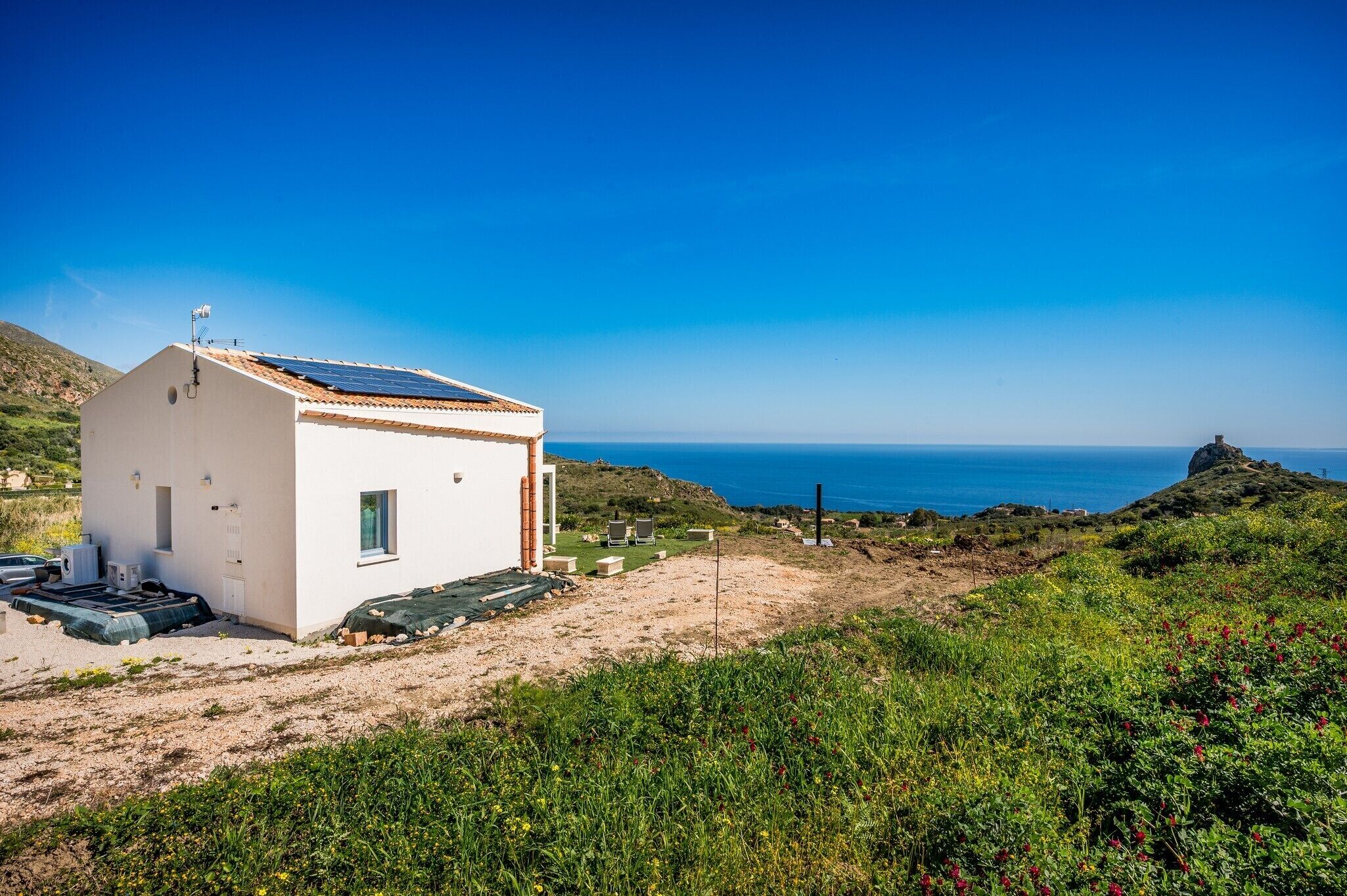A white building with a tiled roof, solar panels, and a small garden area.