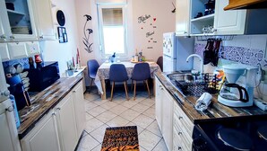 Cocina compacta con gabinetes blancos, un comedor con mesa y sillas, y una isla de cocina con cafetera.