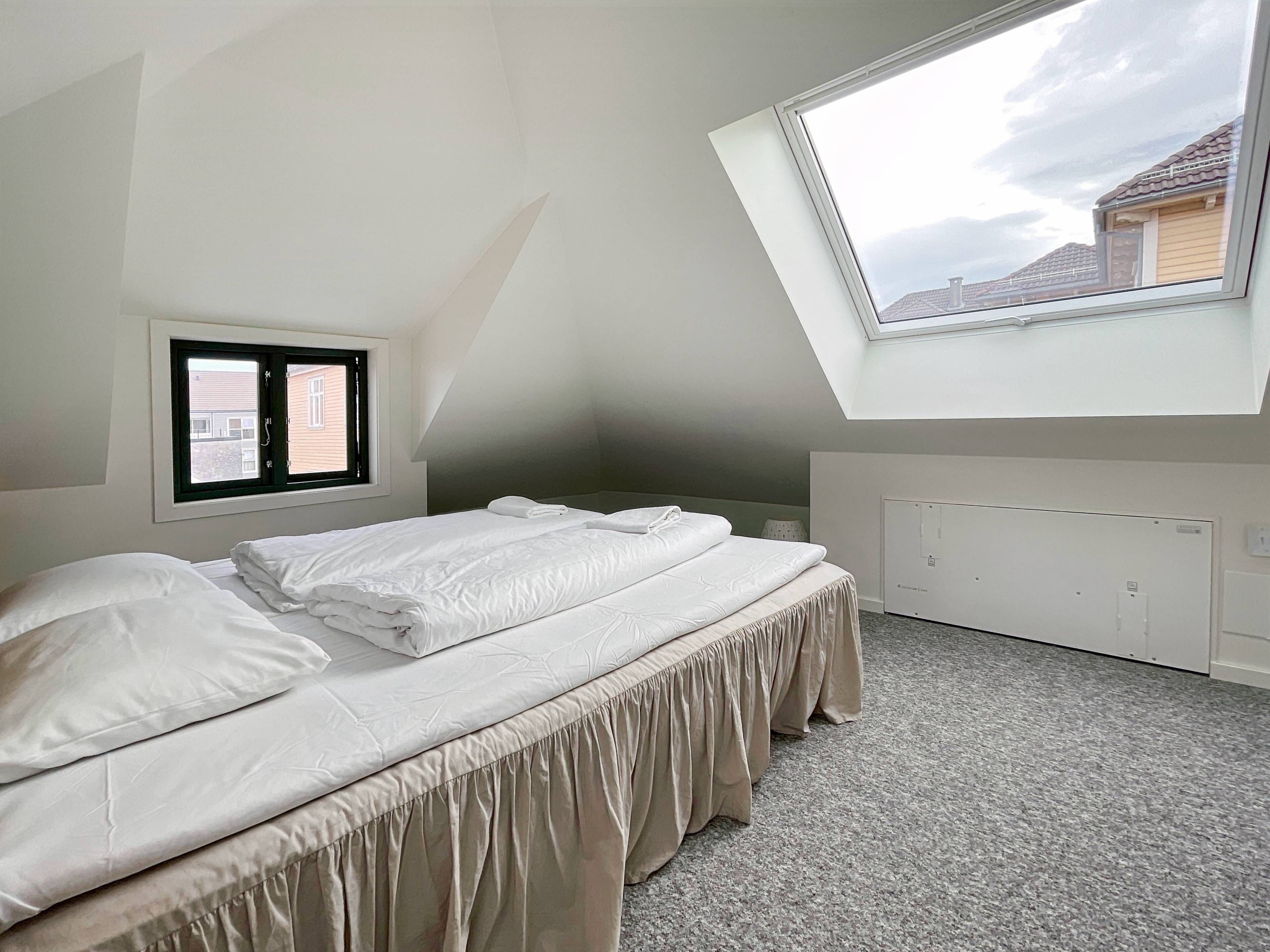 Une chambre avec un puits de lumière, un lit avec une literie blanche, une fenêtre et un radiateur.