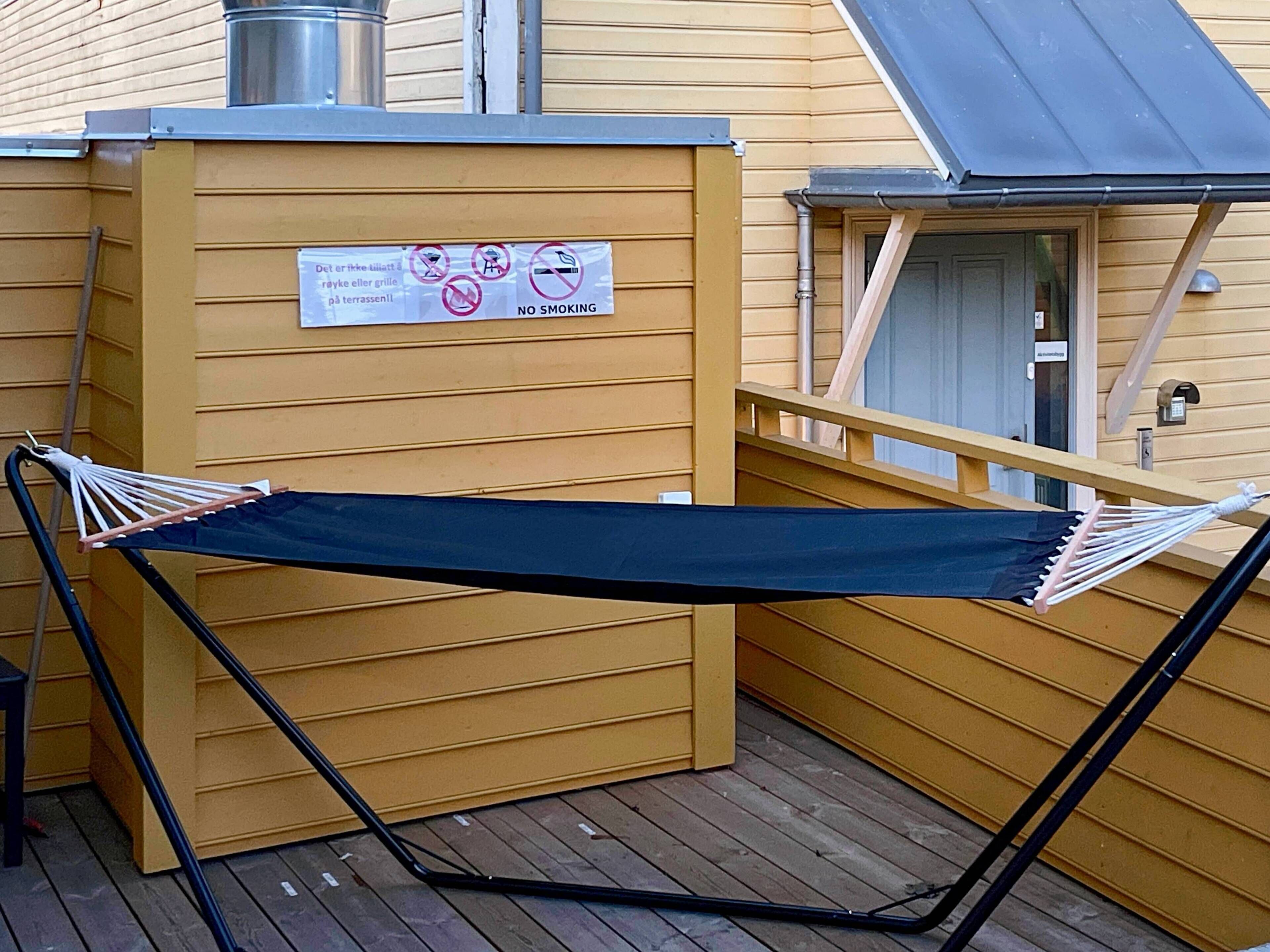 Un hamac sur une terrasse en bois, avec un panneau indiquant qu’il est interdit de fumer sur le bâtiment.