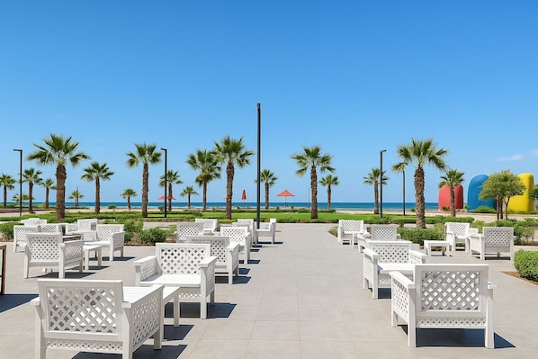 A beachside patio with white outdoor furniture, palm trees, and a clear view of the ocean.