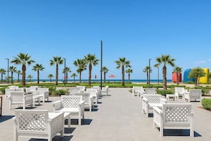 A beachside patio with white outdoor furniture, palm trees, and a clear view of the ocean. - Cozy Coastal Apartment (Al-Manasrah)