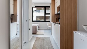 Ein moderner, gut beleuchteter Flur mit Küchenzeile, die Holzschränke, einen weißen Kühlschrank und ein Fenster mit Blick auf Gebäude bietet.