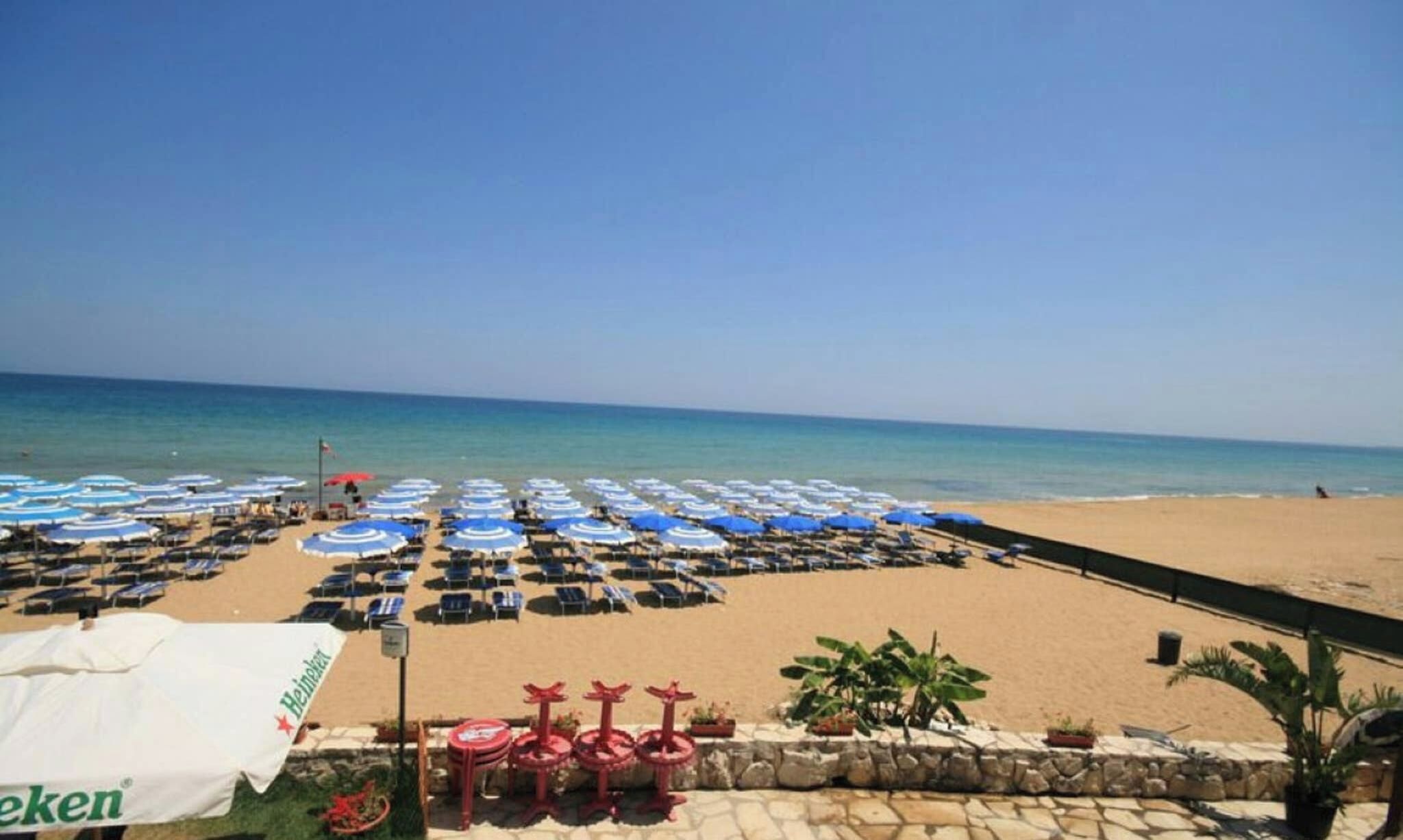 Une plage bordée de rangées de parasols bleus et blancs, de chaises longues et d’une banderole Heineken.
