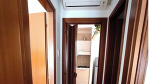 A narrow hallway with wooden doors and a tiled floor, leading to a kitchen area with cabinets and a stove. - Cozy Flat Near the Beach (San Michele al Tagliamento)