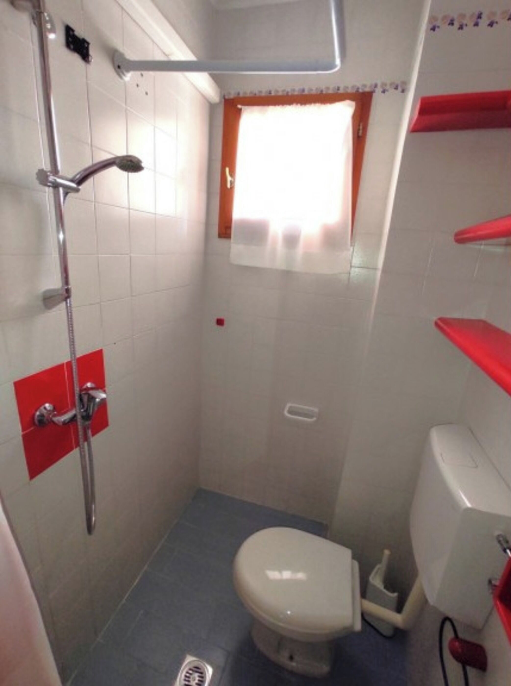 Een kleine, functionele badkamer met douche, toilet en raam.