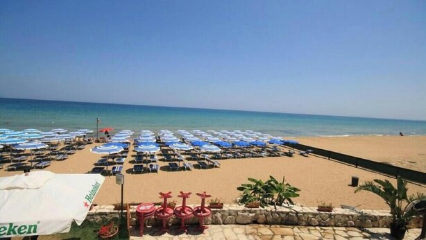 Ein Strand mit Reihen blauer und weißer Sonnenschirme, eine Mauer mit Pflanzkübeln und ein Schild für Heineken.