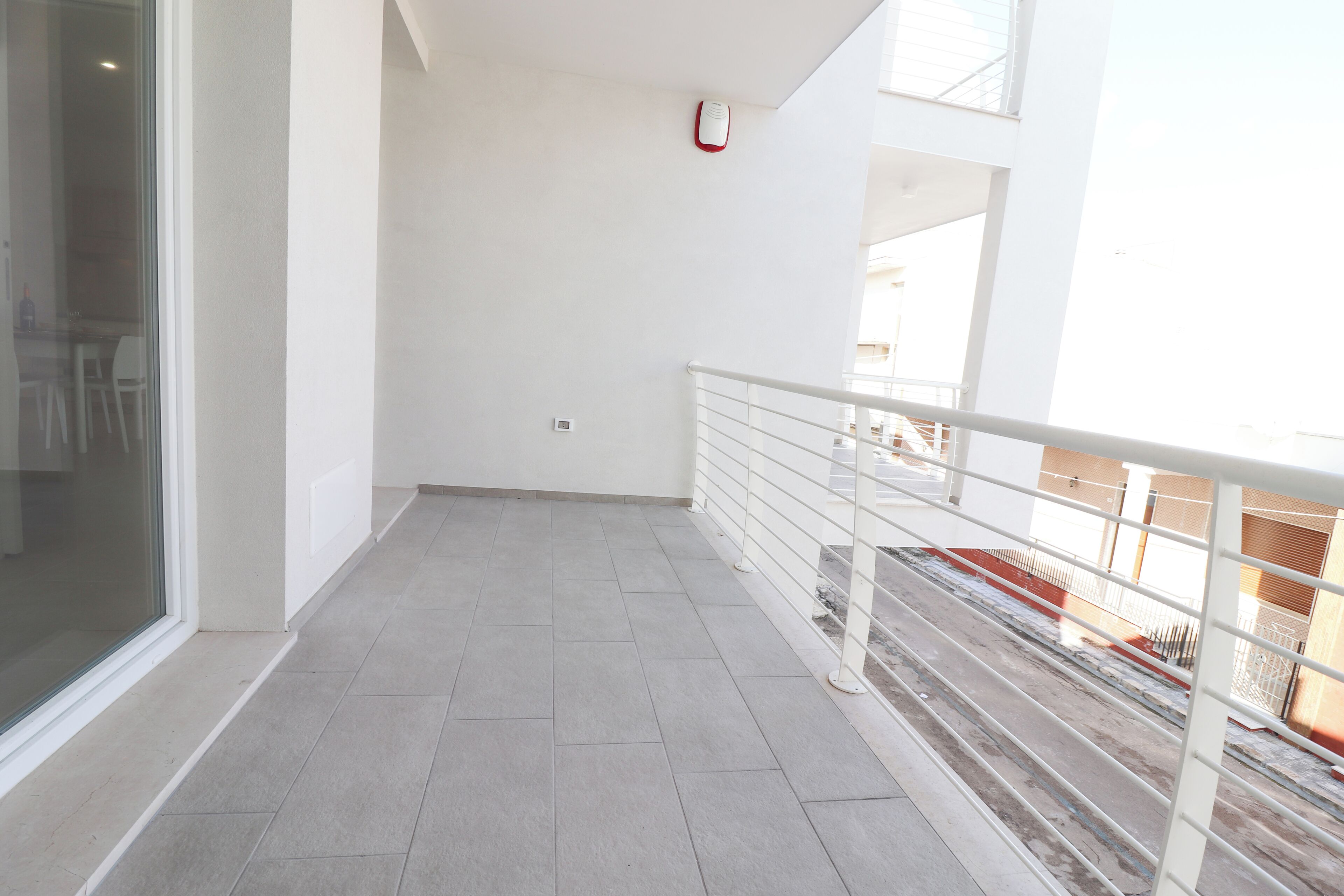 A balcony with a tiled floor, white walls, and a glass door.