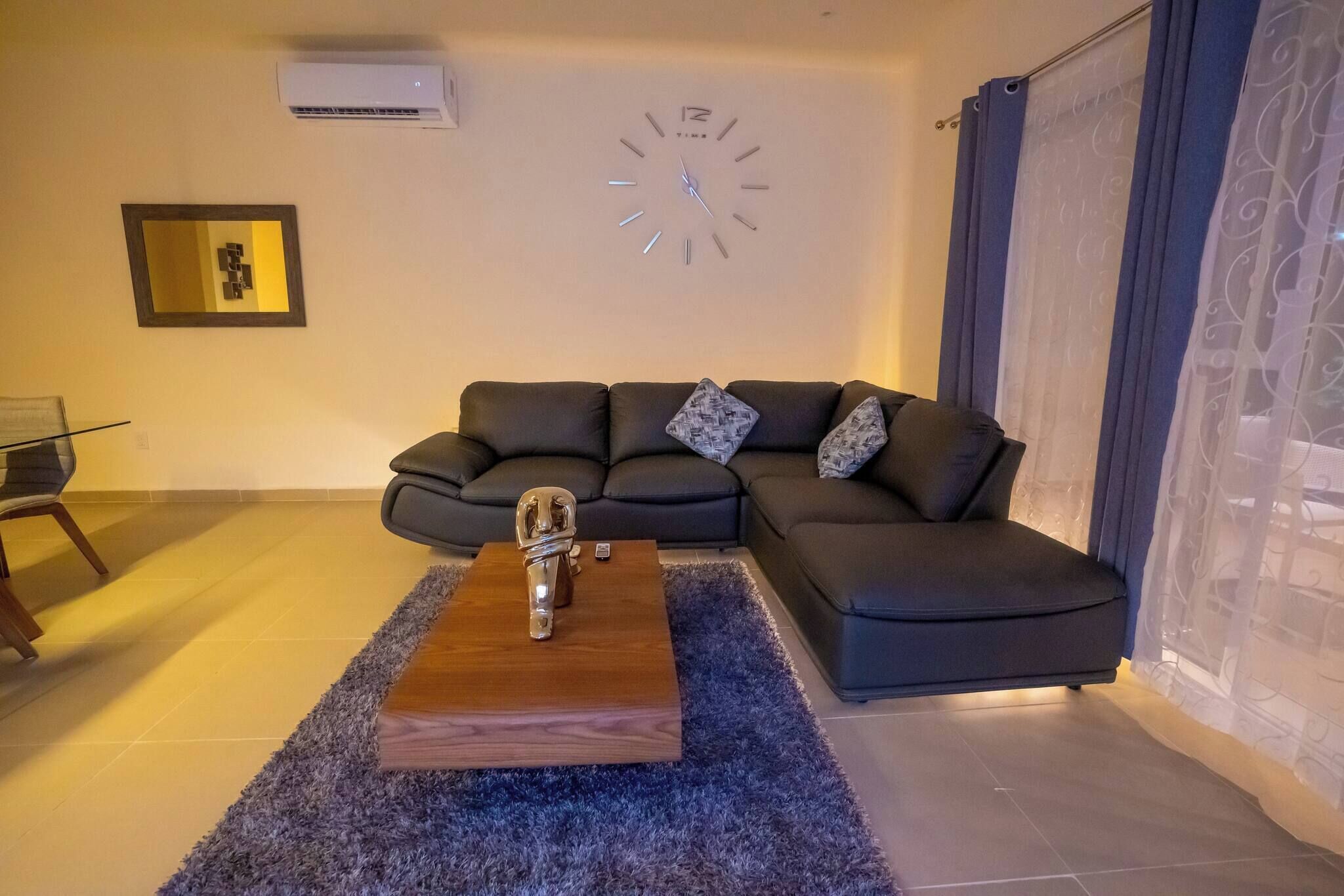 A modern living room with a sectional sofa, a wooden coffee table, a wall clock, and a mirror.