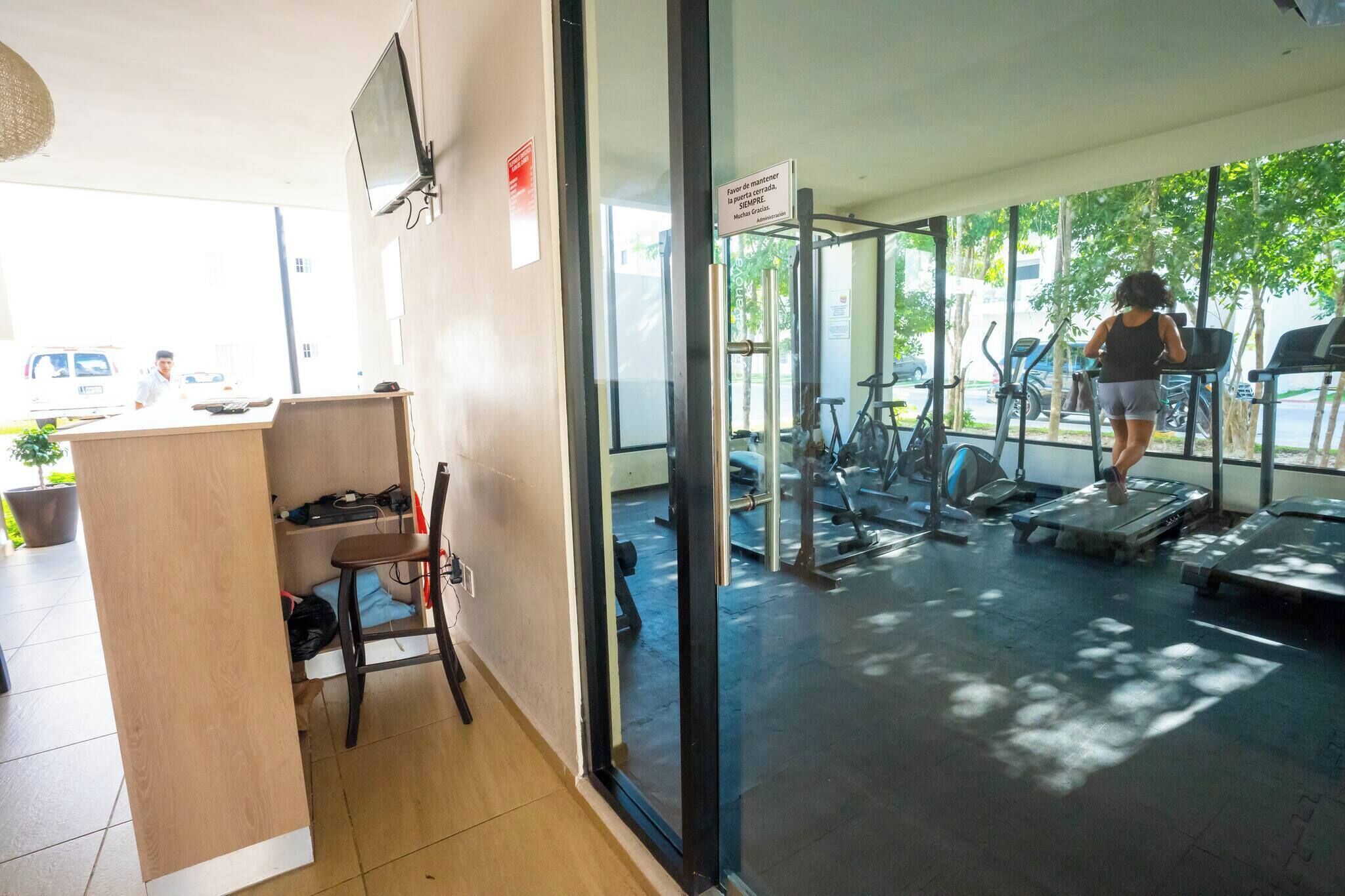 A gym with exercise equipment, a reception desk, and a view of the outside.