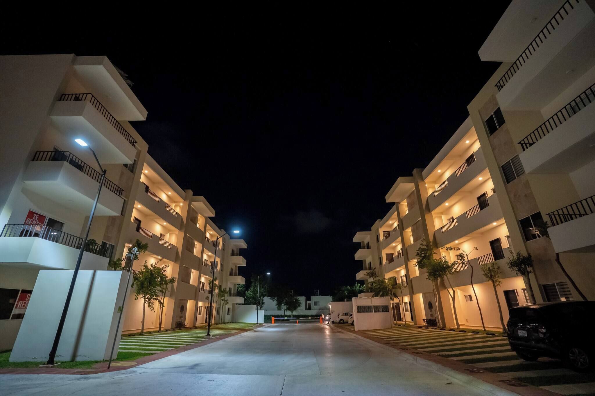 A multi-story residential building with balconies, a gated entrance, and a clear night sky.