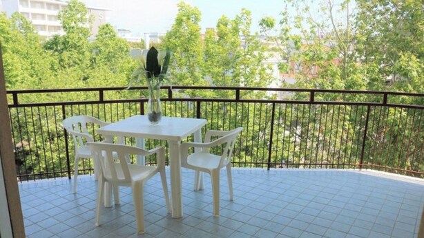 A balcony with a tiled floor, a white table with four chairs, and a potted plant.