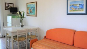 A room with a white dining table, orange sofa, and two paintings on the wall.