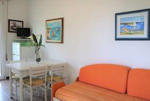 Ett rum med ett vitt bord, en orange soffa och två tavlor på väggen.