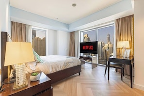 Ein Hotelzimmer mit Bett, Schreibtisch mit Computer, Fernseher mit Netflix und Blick auf die Stadt.