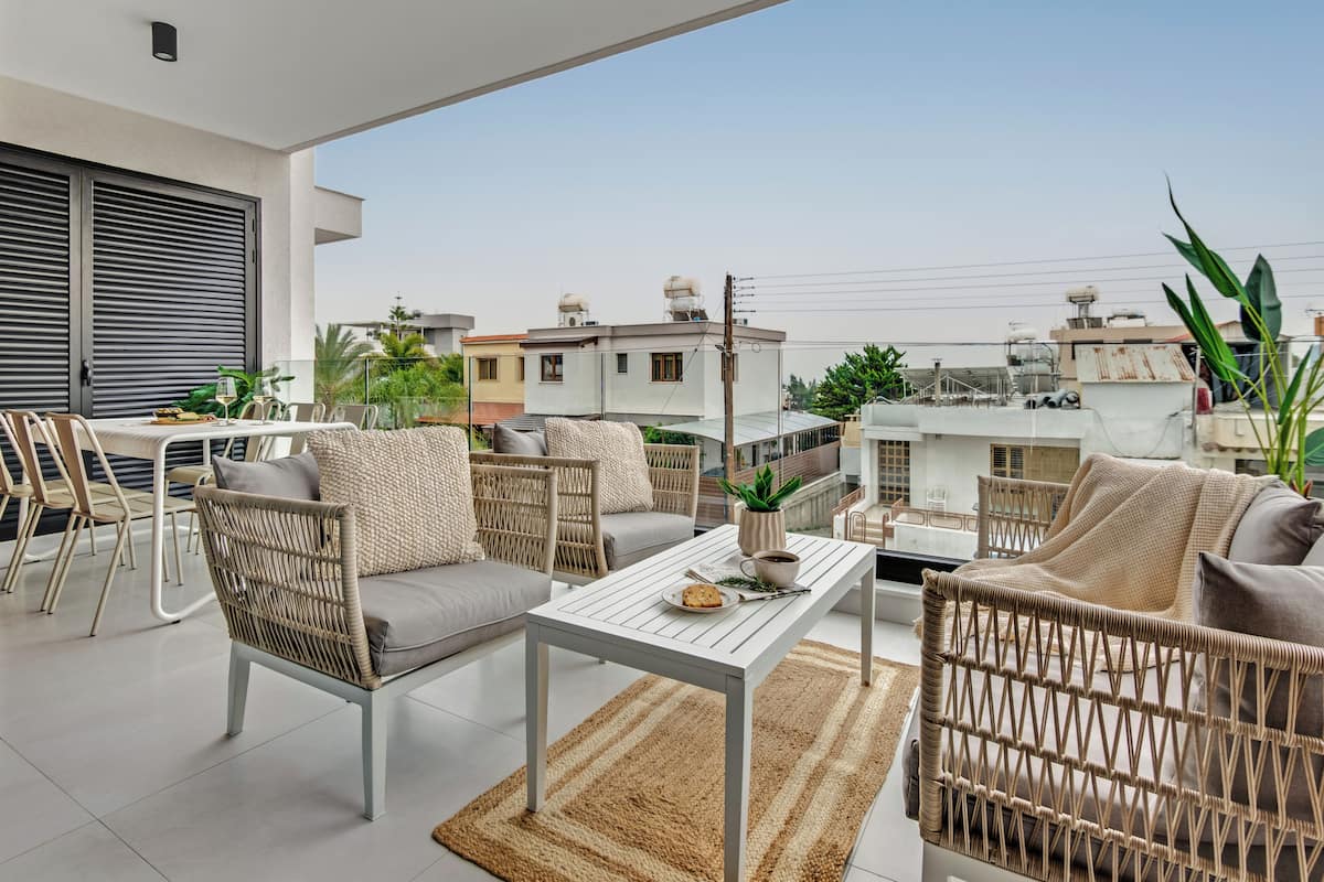 A rooftop terrace with wicker furniture, a dining table, and potted plants.